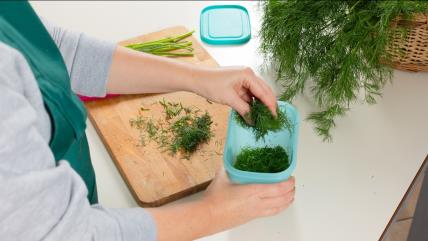 Osoba stavlja seckano začinsko bilje u plastičnu kutiju