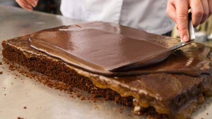 Poslastičar maže čokoladnu glazuru preko kolača