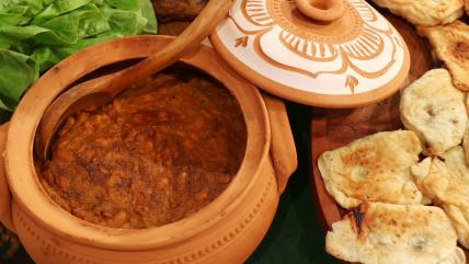 Prebranac u zemljanoj posudi na stolu sa lepinjicama i salatom