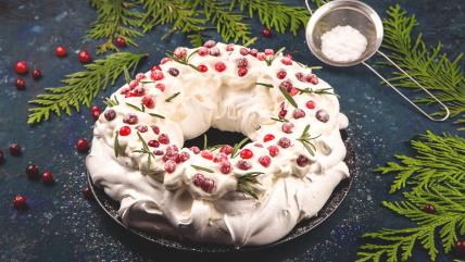 Božićni pavlova venac sa bobičastim voćem posut prah šećerom na stolu