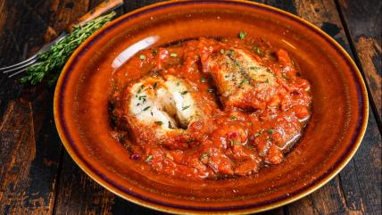 Riba oslić u paradajz sosu sa belim lukom u tanjiru na stolu