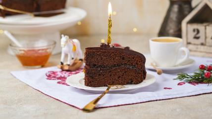 Saher torta na tanjiru sa svećicom na stolu, okružena božićnim ukrasima