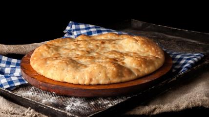 Presna pogača na dasci na plehu pored krpe na plavo bele kockice