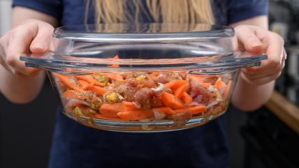 Žena drži vatrostalnu posudu sa povrćem i mesom