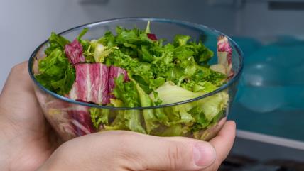 Osoba stavlja činiju sa zelenom salatom u frižider