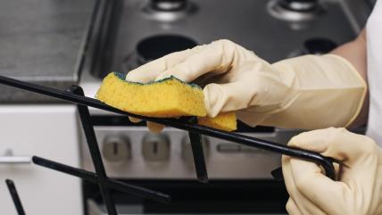 Žena čisti sunđerom rešetke sa šporeta na gas